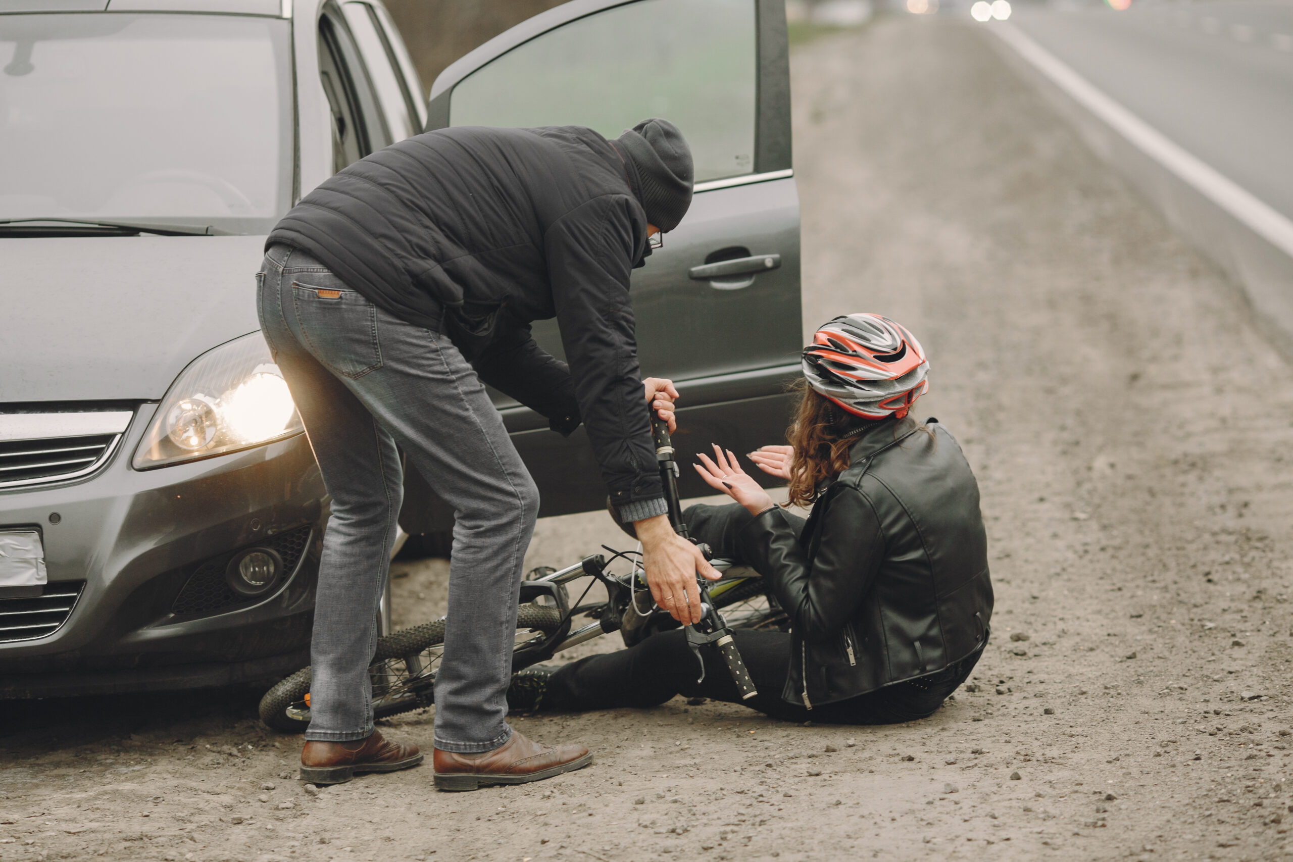 A good samaritan driver stops to help an injured bicyclist on the side of the road.