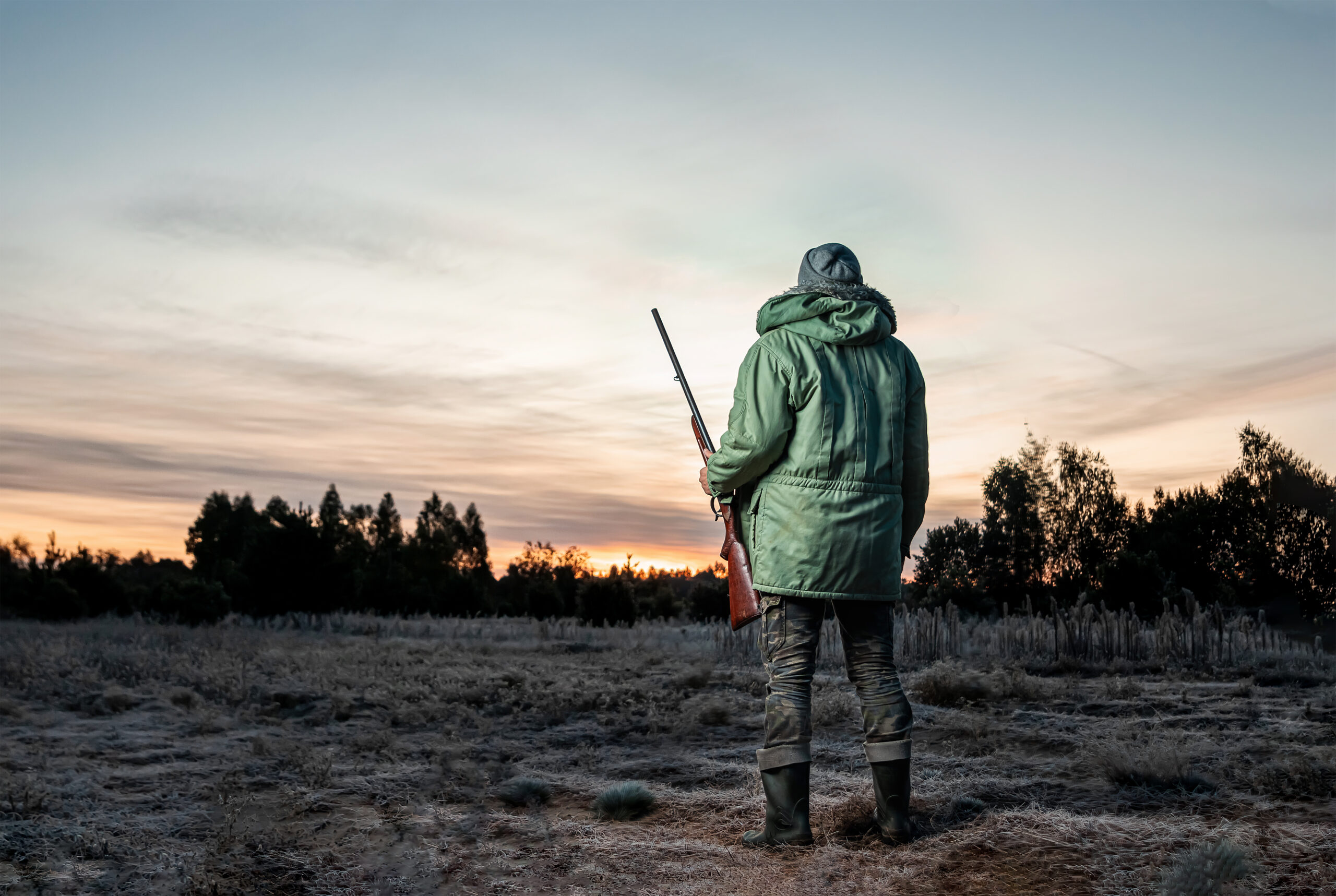 Hunter man in camouflage with a gun during the hunt in search of wild birds or game on a beautiful sunset. The concept of a hobby, killing.