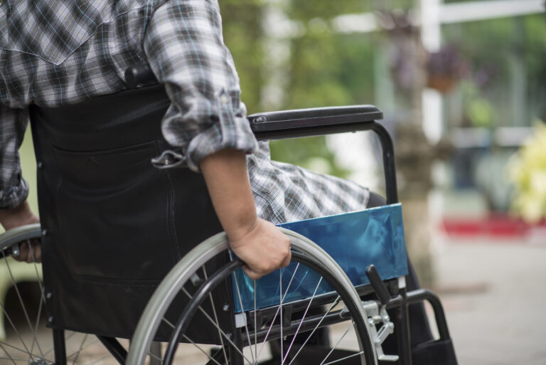 Close-up of senior woman hand on wheel of wheelchair during walk
