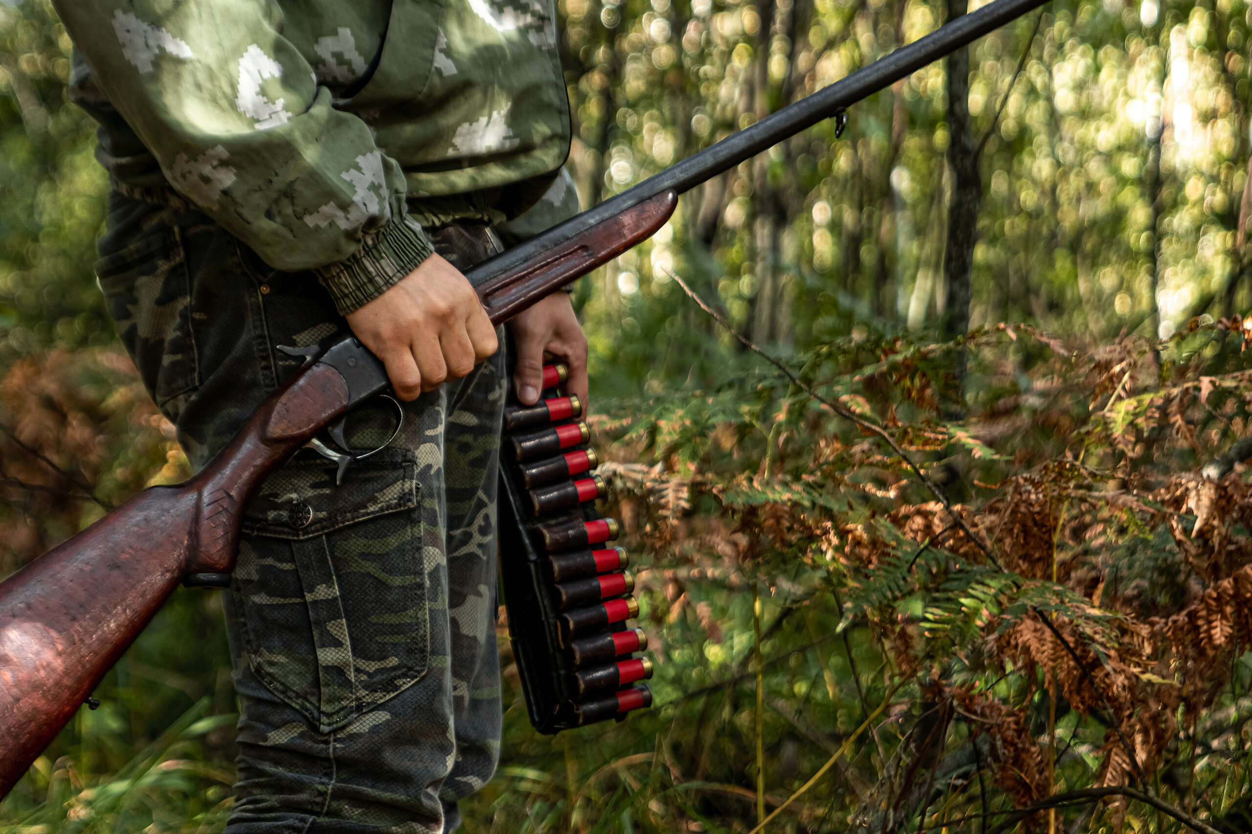 A hunter in the woods with a shotgun and shells.