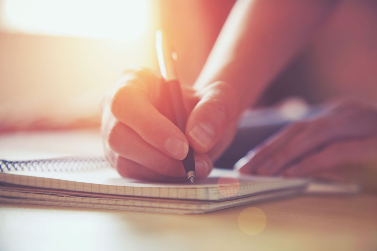 Close up of a woman writing in a journal with a pen.