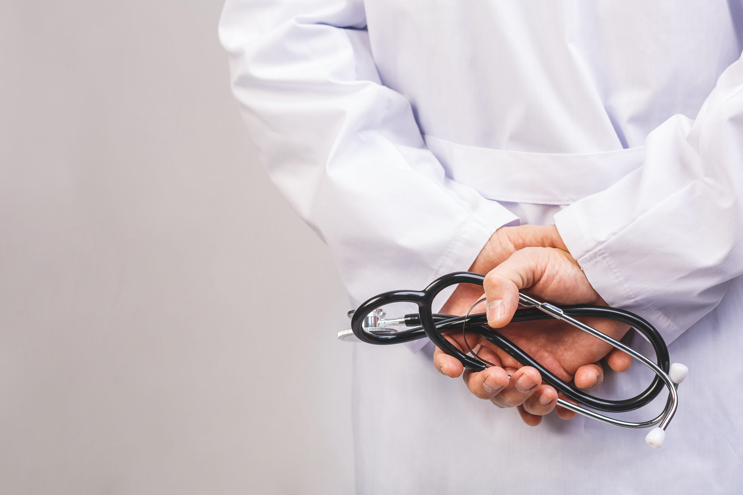 A doctor in a white lab coat holds his hands and a stethoscope behind his back.