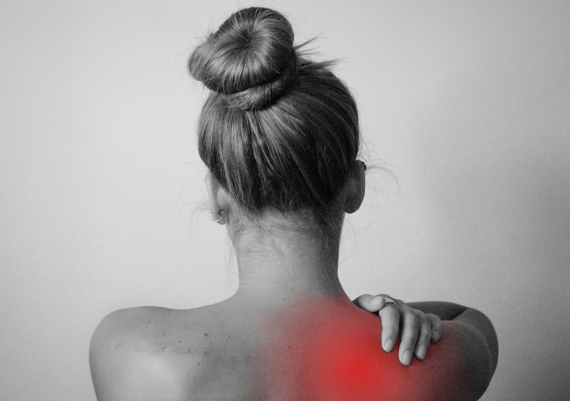 black and white photo of a woman from behind rubbing her right shoulder the center of the pain in her shoulder is highlighted in red