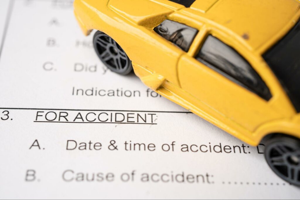 Close up of a car accident insurance reporting form with a decorative toy car on top of it. Filing a claim accurately is key for injured passengers to get the compensation they need.