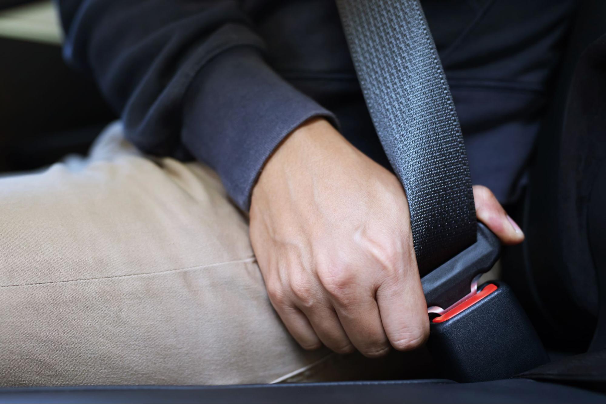 Close up of a passenger in a car buckling his seatbelt.