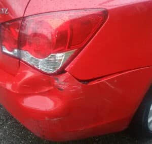 Red car with damage to the rear bumper and taillight area, showing dents and scratches.