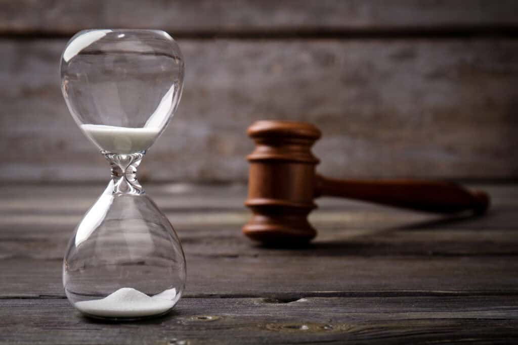 An hourglass with sand partially run through is placed beside a wooden gavel on a wooden surface.