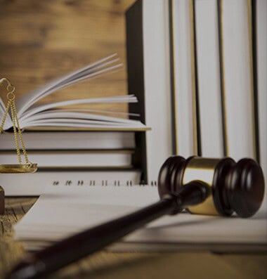 Wooden gavel and scales of justice on a desk with open and closed books in the background.