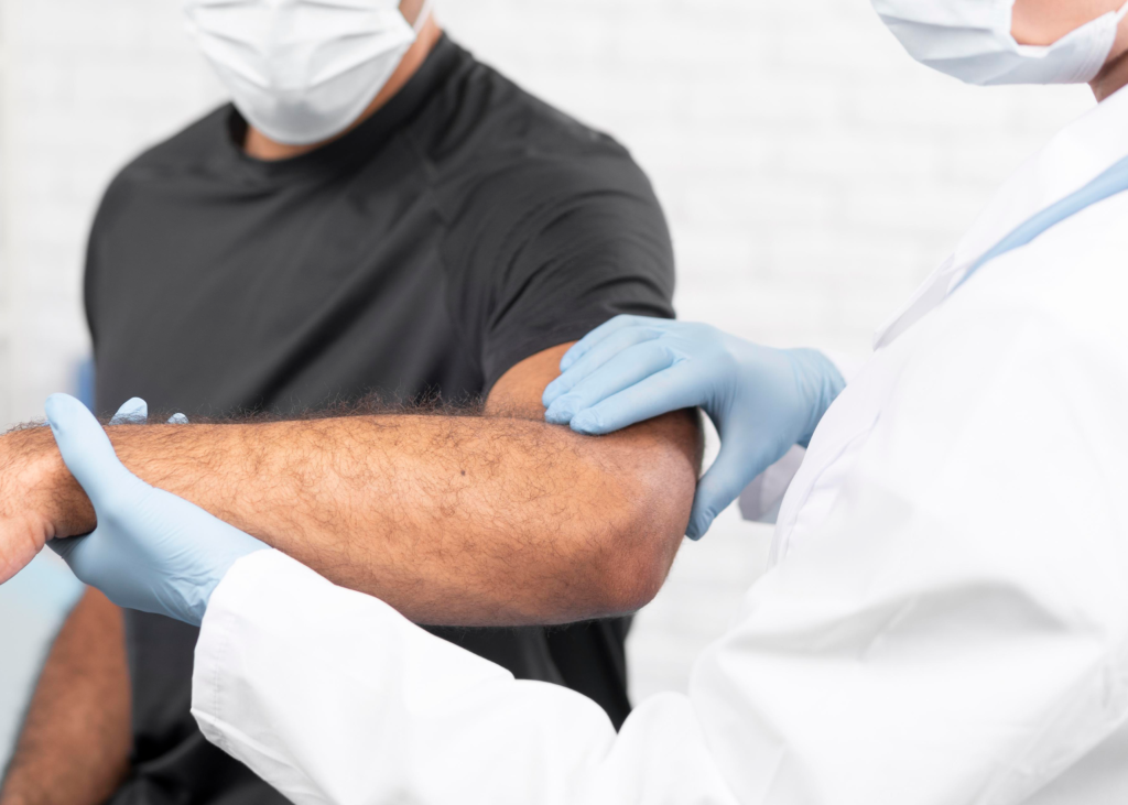 A healthcare professional examines a patient's arm while both wear face masks and gloves.