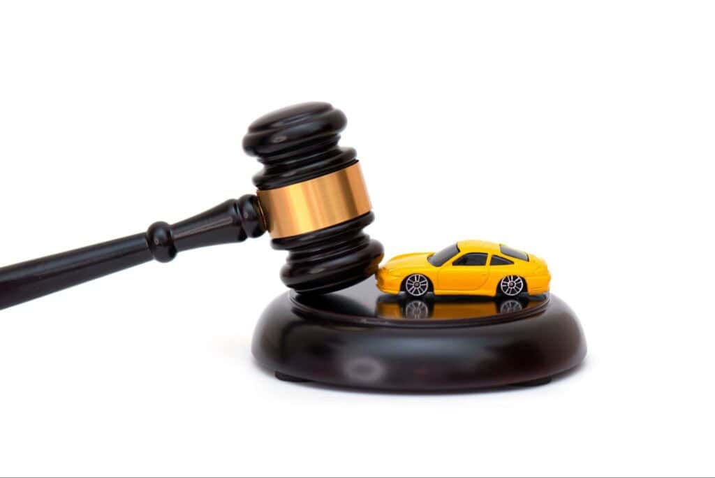 A yellow toy car is placed beneath a black and gold judge's gavel on a white background.