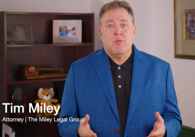 A man in a blue checkered blazer stands in an office, speaking. Text reads: "Tim Miley, Attorney, The Miley Legal Group." Books and decor are visible on a shelf in the background.