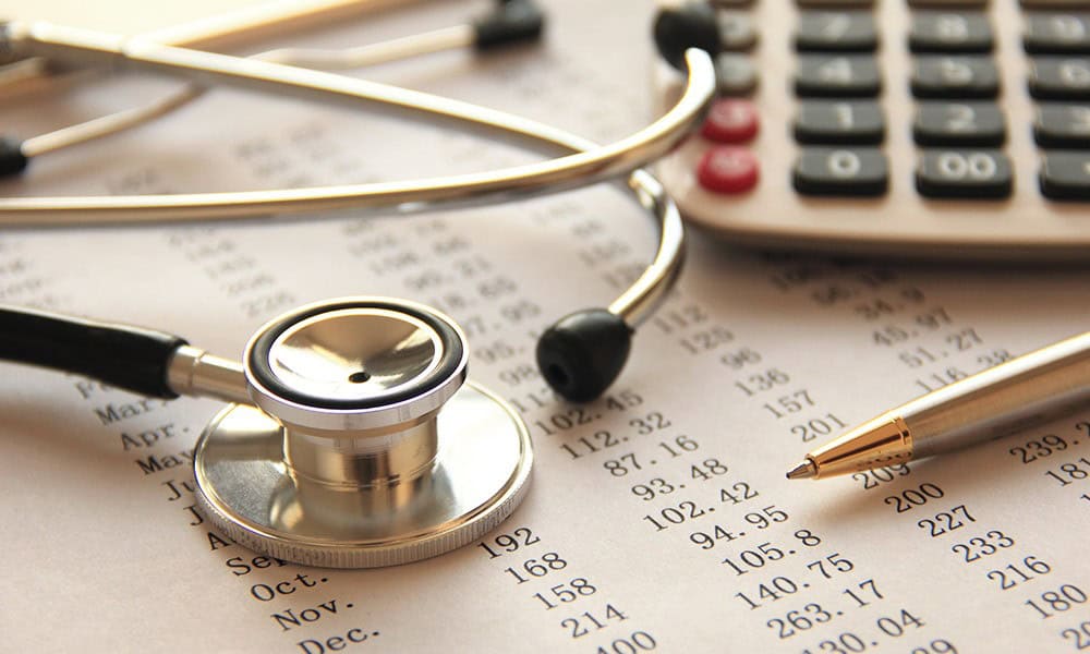 A stethoscope, pen, and calculator on financial documents with numbers.