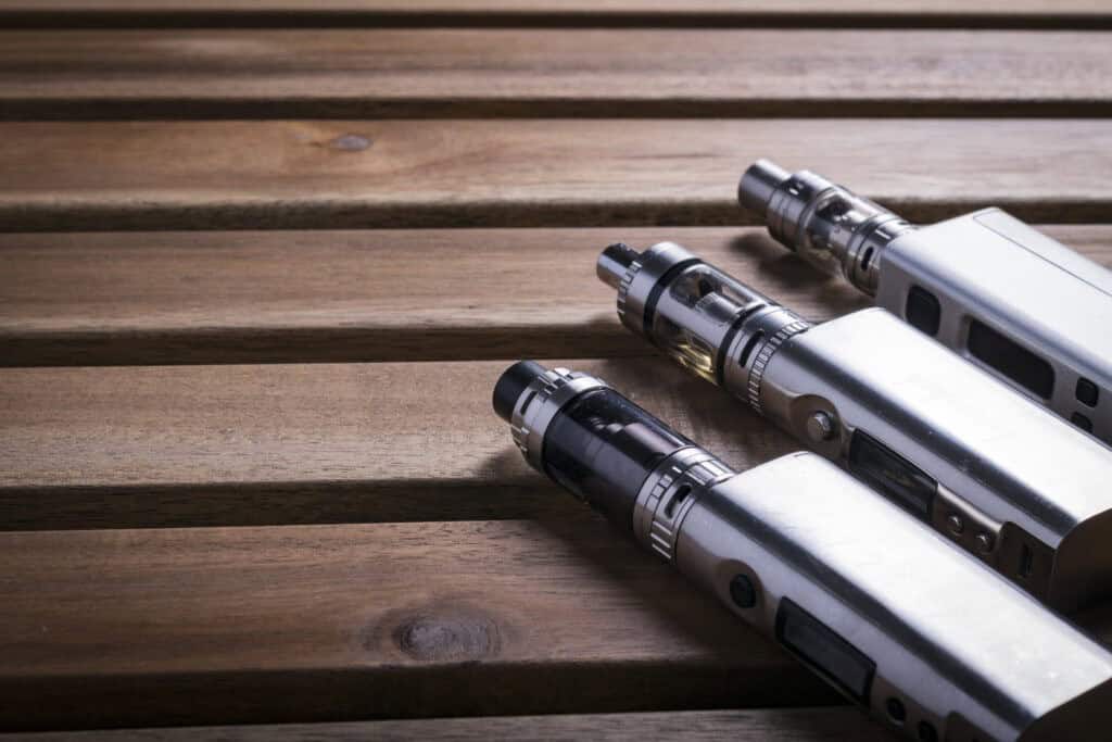 Three silver vaping devices are placed in a row on a wooden surface.