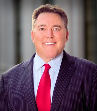 Man in a pinstripe suit and red tie smiles at the camera.