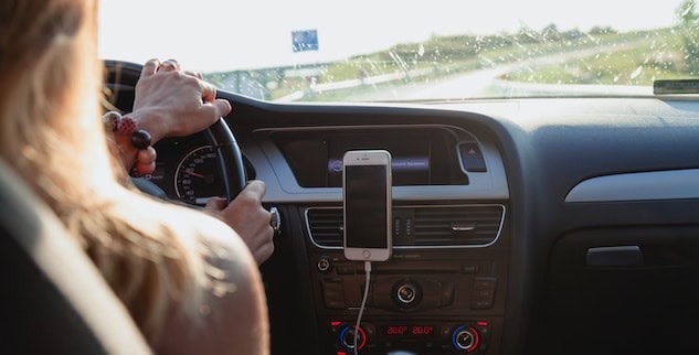 Driver with hands on the steering wheel, smartphone mounted on the car dashboard, and a view of the road ahead.