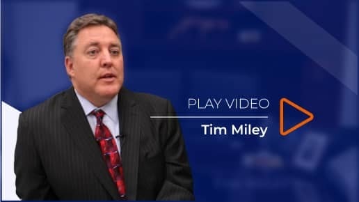 A person in a suit sitting against a blue background with the text "Play Video" and a play icon beside the name "Tim Miley.