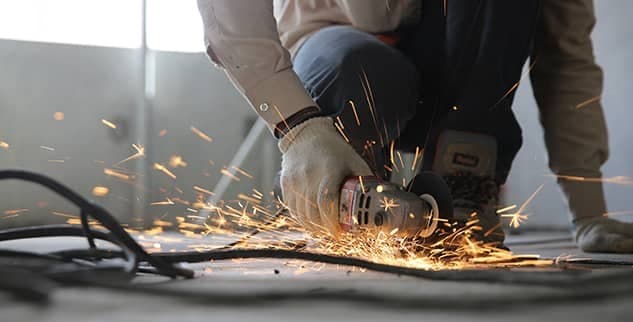 A person using an angle grinder emits sparks while cutting through metal on the floor.