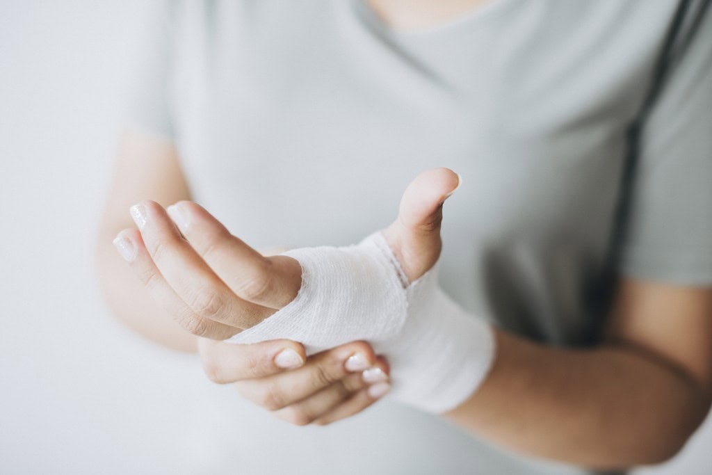 Person with a bandaged hand holding their injured wrist, wearing a gray shirt.